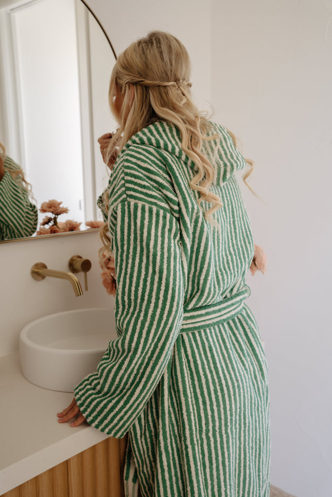 Woman in a green and white striped robe standing in a bathroom.