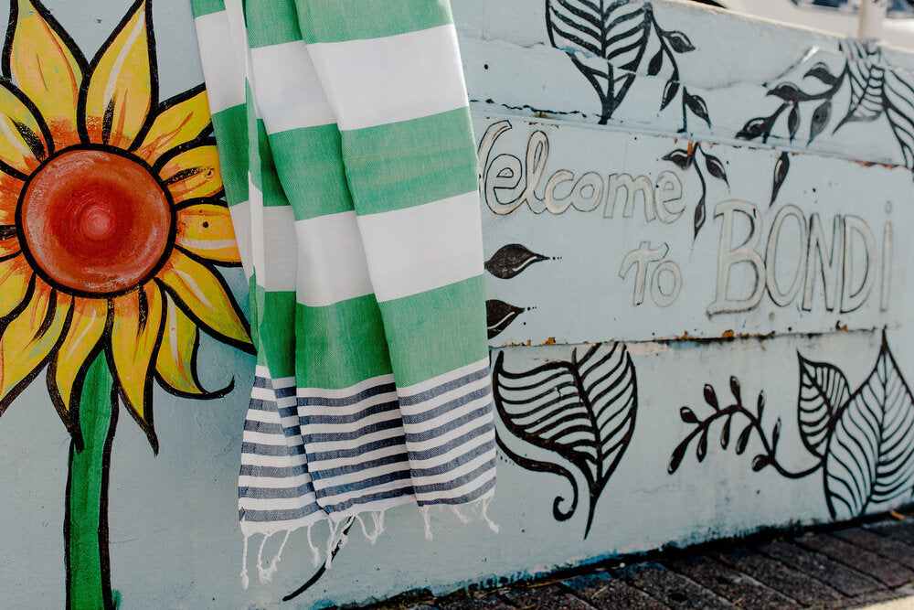 Apple green and navy striped Flamenco Turkish towel with fringes hanging by mural