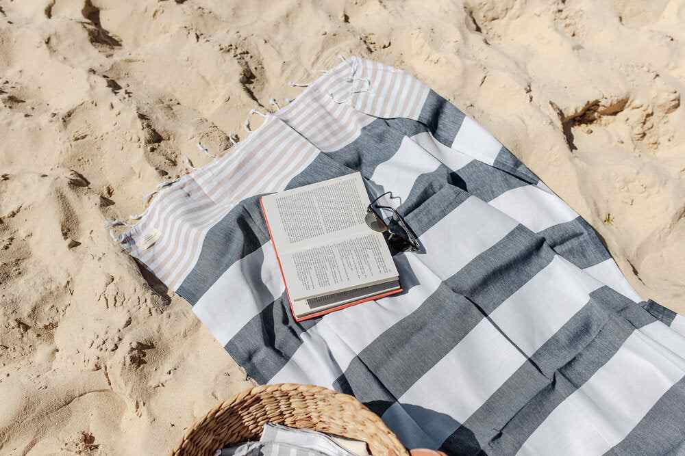 Navy and beige striped Flamenco Turkish towel with book and sunglasses on sandy beach