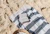 Navy and beige striped Flamenco Turkish towel with book and sunglasses on sandy beach