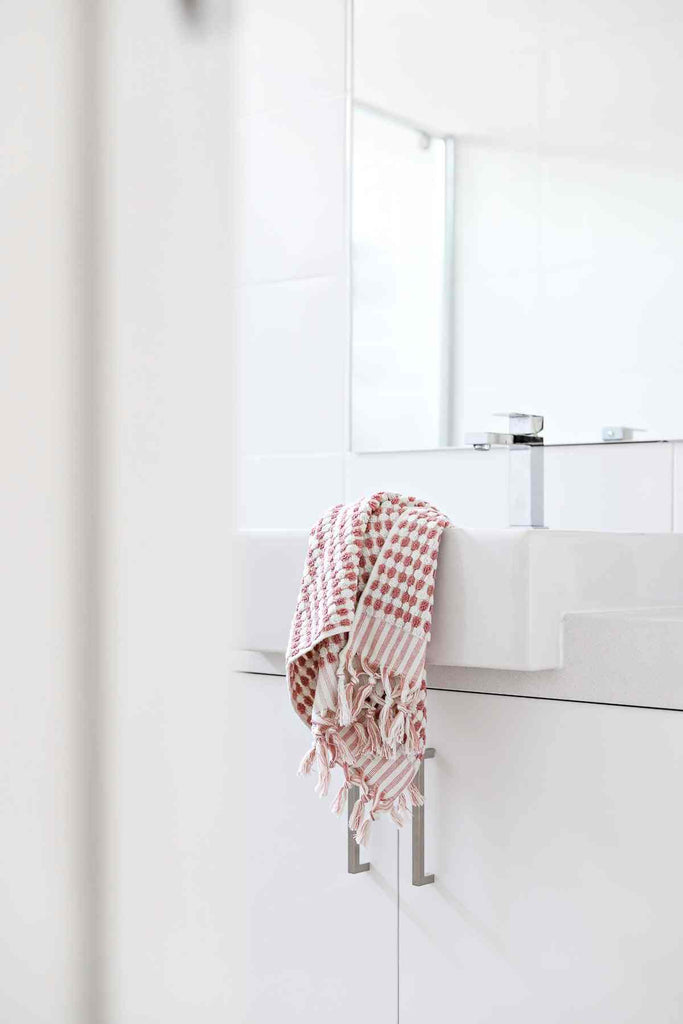Pink Turkish cotton towel with pompom detail hanging in modern bathroom