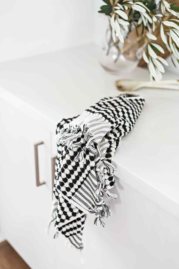 Black and white pompom Turkish cotton hand towel with tassels on white countertop