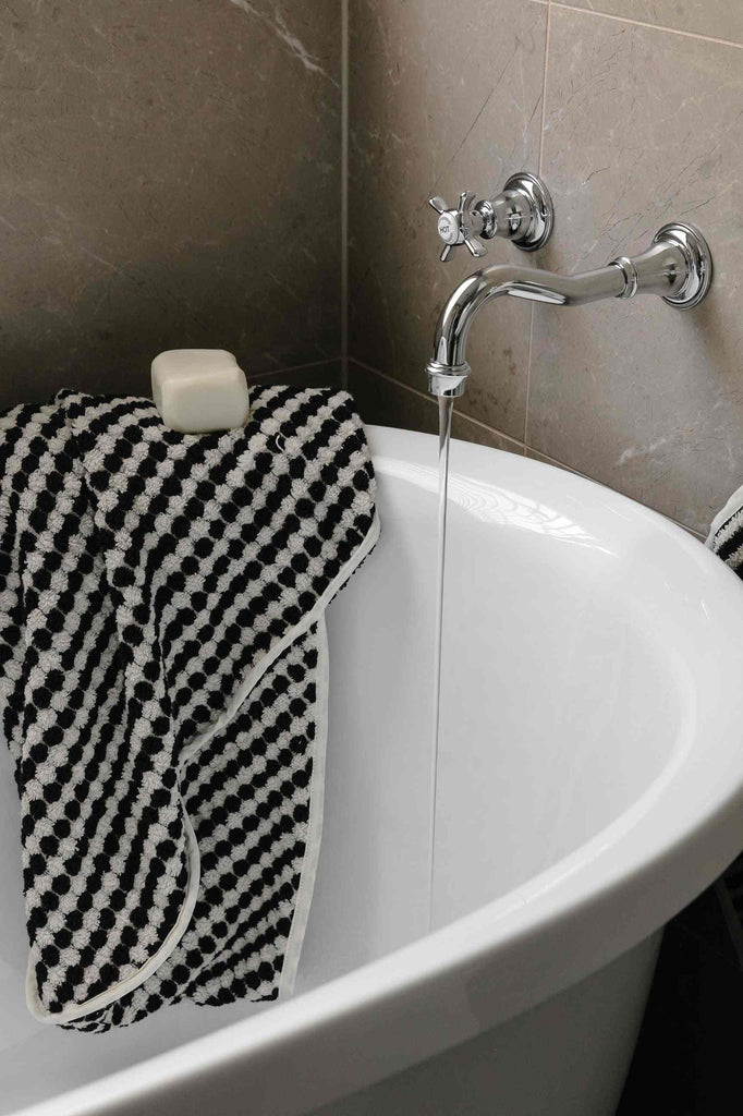 Black and white pompom Turkish cotton hooded baby towel on bathtub edge